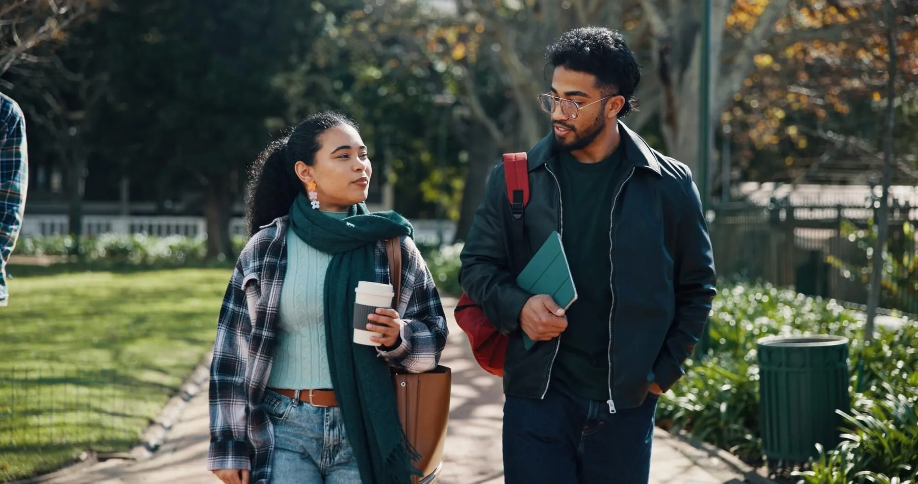 Dos estudiantes universitarios conversan mientras caminan por el campus con un café y sus cuadernos